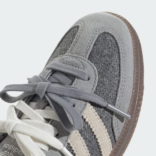 Hands holding an open shoebox containing a grey low-top trainer in tissue paper, representing a limited UK sneaker drop unboxing